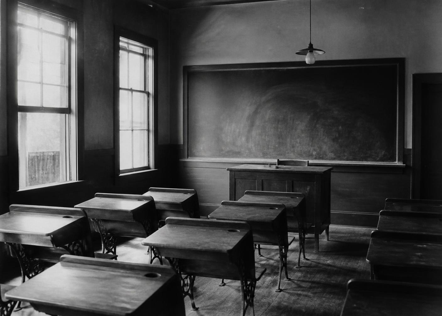 Salle de classe ancienne, pupitres en bois face à un grand tableau noir